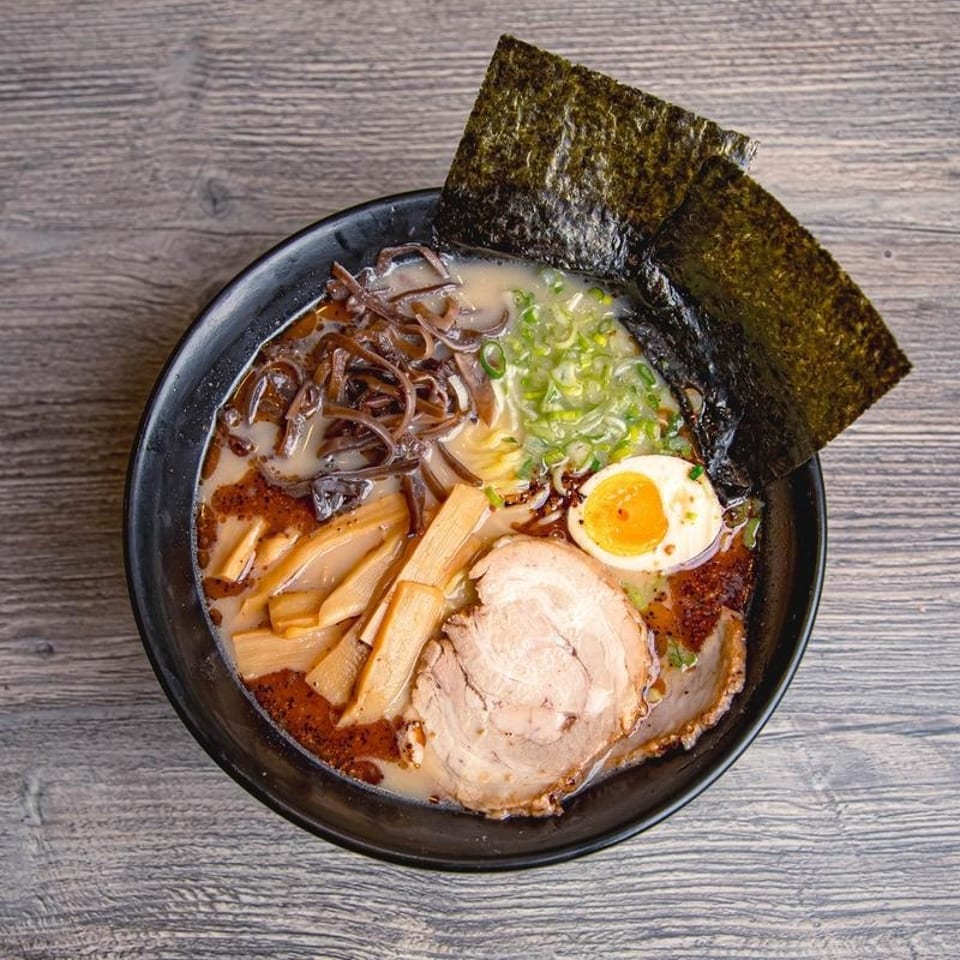 Overhead view of ramen with pork, soft-boiled egg, bamboo shoots, mushrooms, scallions, and seaweed in a black bowl.