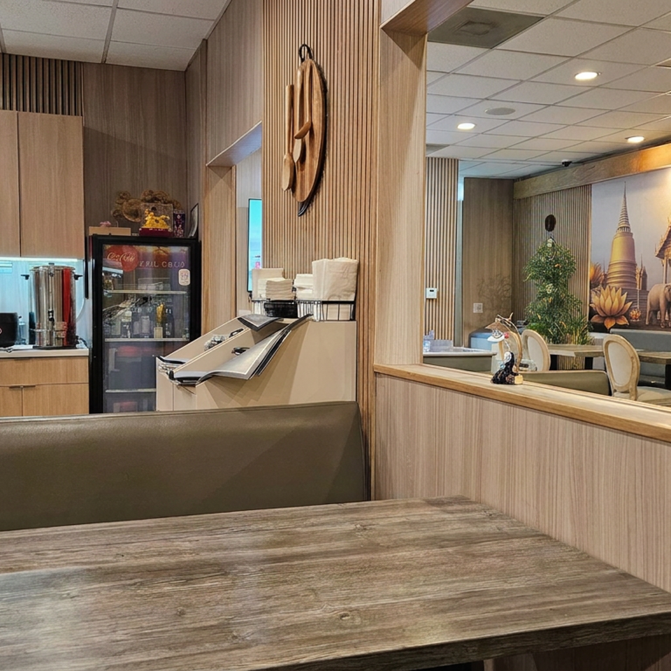 Warmly lit restaurant interior with wooden tables, booth seating, open kitchen counter, and Thai temple mural.