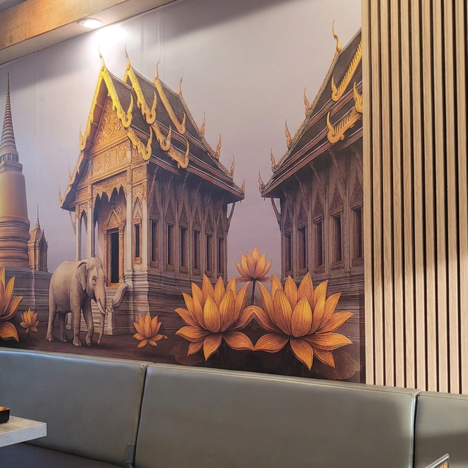 Restaurant dining area featuring Thai temple mural with elephants and lotus flowers, wood paneling, booth seating, and dishes on a table.
